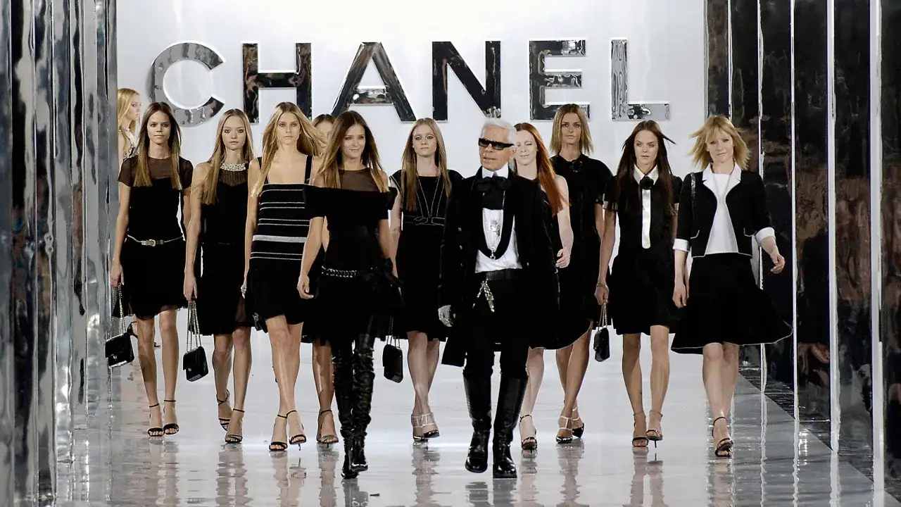 Sfilata Chanel con Karl Lagerfeld e modelle in abiti neri. Le frasi Coco Chanel risuonano nell'eleganza senza tempo.