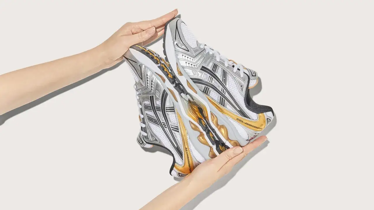 Mani che sorreggono scarpe da ginnastica Asics argentate e dorate, un esempio di design innovativo dell'azienda.