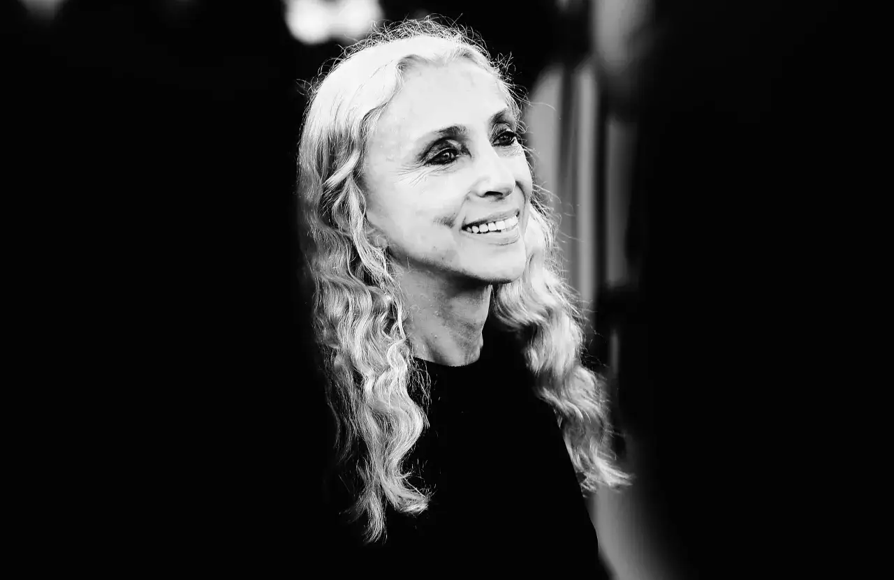 Ritratto in bianco e nero di Franca Sozzani, con lunghi capelli biondi mossi e un sorriso radioso.