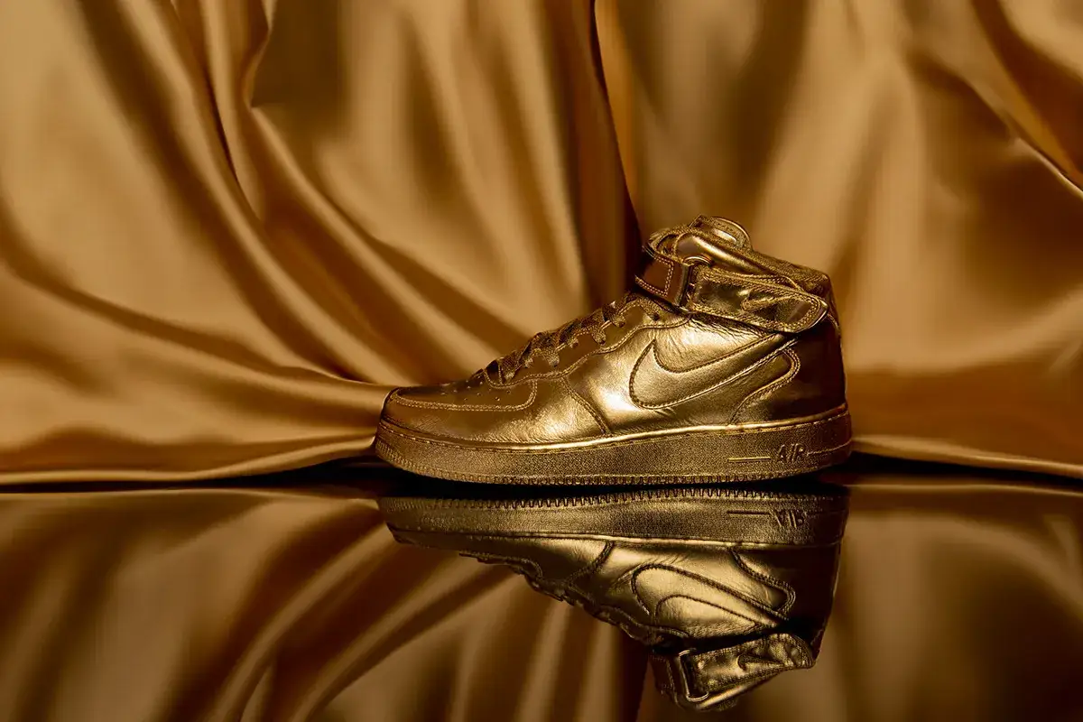 Scarpa Nike Air Force 1 dorata, lucida e riflettente, su sfondo di seta color oro. Un vero tesoro, tra le scarpe più costose al mondo.