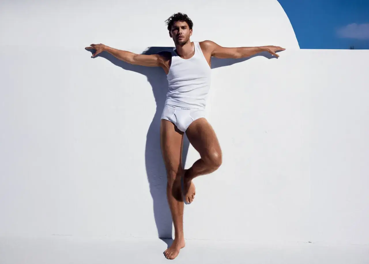 Modello in intimo Calvin Klein, con le braccia aperte contro un muro bianco. L'iconico stilista Calvin Klein celebra la forma maschile.