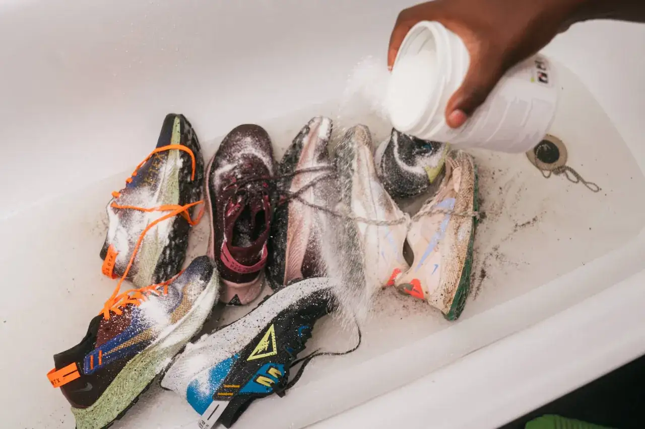 Un contenitore bianco versa polvere su diverse scarpe da ginnastica in una vasca, un modo per disinfettare scarpe usate.