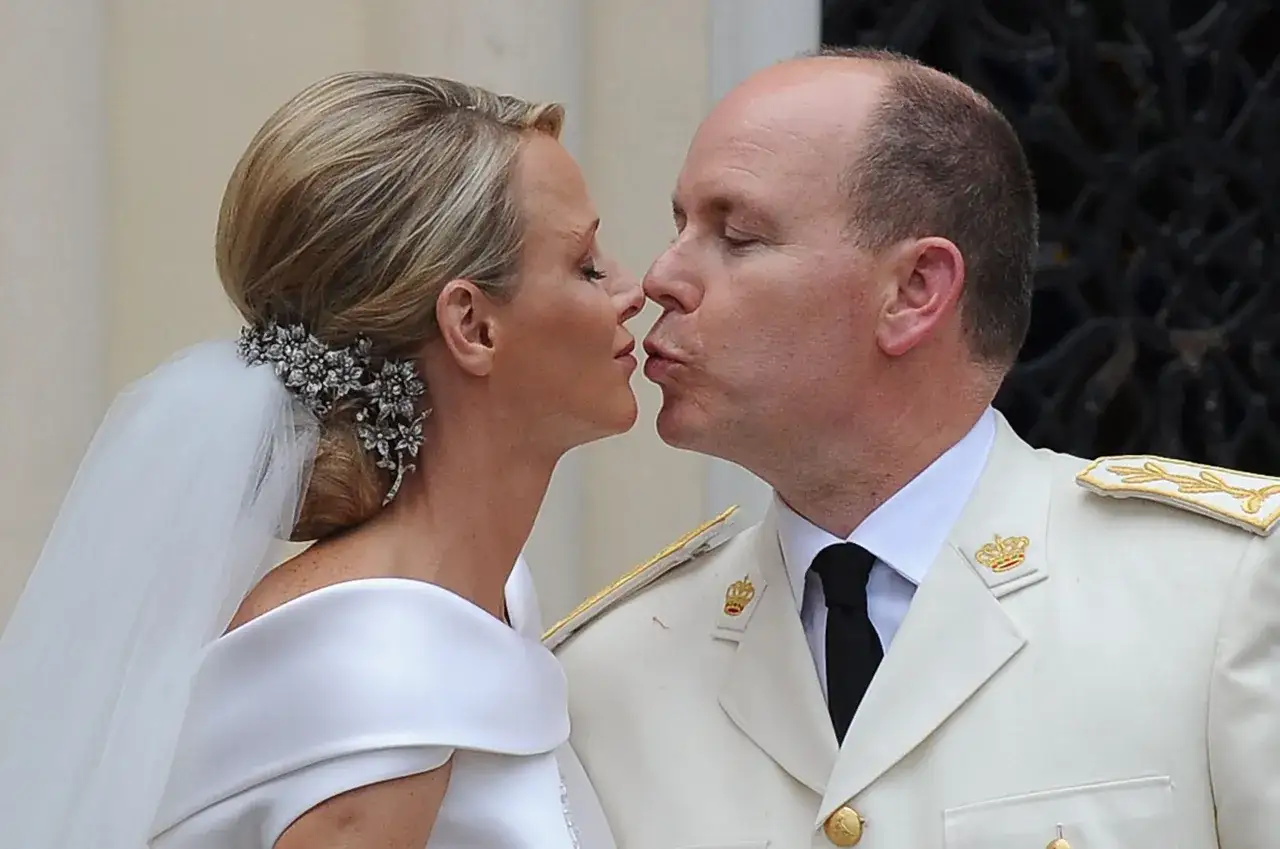 Charlene di Monaco e Alberto II si baciano, lei con un velo da sposa e un prezioso fermaglio, lui in uniforme.