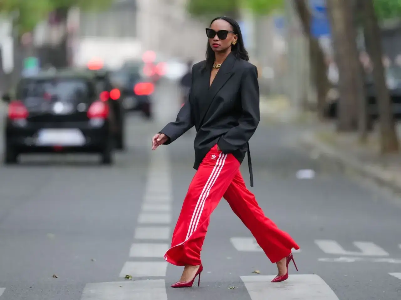 Donna attraversa la strada con pantaloni rossi Adidas e blazer nero. Un look audace per capire come abbinare pantaloni rossi.