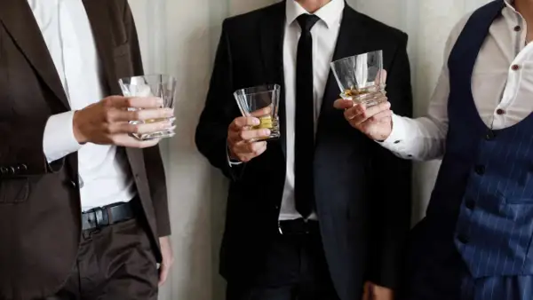 Uomini eleganti con bicchieri di whisky, perfetti per un dress code cocktail.