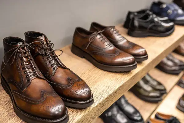 Vari tipi di scarpe eleganti in pelle marrone e nera, con dettagli traforati, disposte su scaffali di legno.