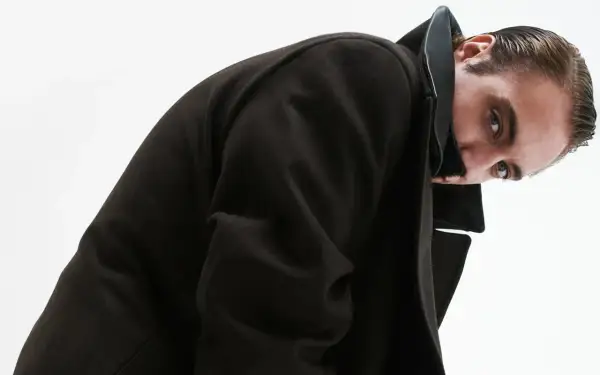 Luca Vergoni, con un cappotto scuro e un'espressione enigmatica, guarda verso l'obiettivo.