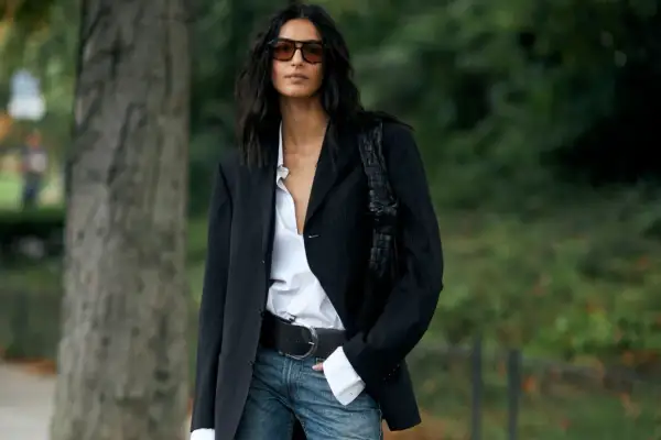 Donna con blazer gessato, camicia bianca sbottonata e jeans. Un look chic e casual.
