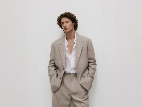 Uomo con giacca beige e camicia bianca sbottonata: un'idea di cosa mettere sotto la giacca uomo per un look casual-chic.