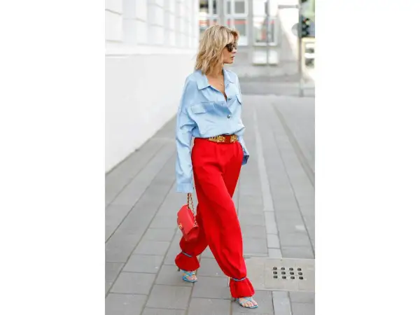 Donna con pantaloni rossi ampi e camicia azzurra, borsa rossa e sandali blu. Un look audace per scoprire come abbinare pantaloni rossi con stile.
