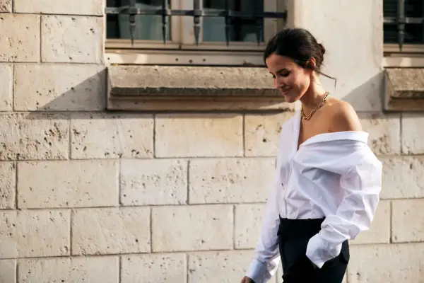Donna con camicia bianca oversize e pantaloni neri, un look smart casual con una collana dorata.