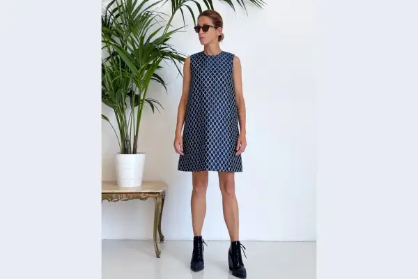 Donna con occhiali da sole indossa un vestito a trapezio blu con fantasia geometrica bianca. Un look moderno che sta bene a molte fisicità.