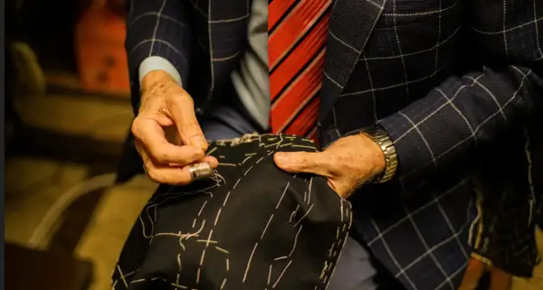 Sarto esperto cuce a mano, mostrando diversi tipi di polsini camicia. Dettagli sartoriali e precisione.