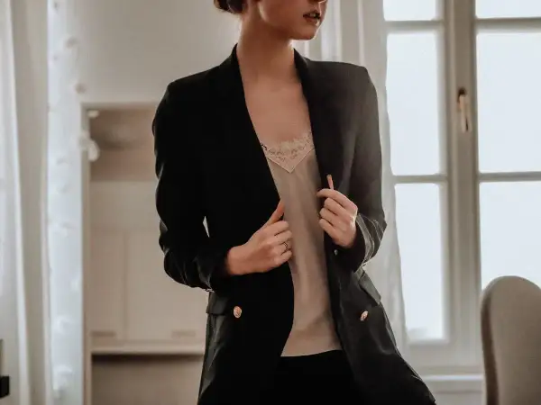 Donna con tailleur nero, indossa una camicetta di pizzo color crema sotto. Un'idea su cosa mettere sotto un tailleur nero.