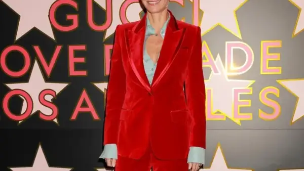 Gwyneth Paltrow in un completo rosso di velluto, sorride davanti a uno sfondo con stelle e lettere rosa e oro.