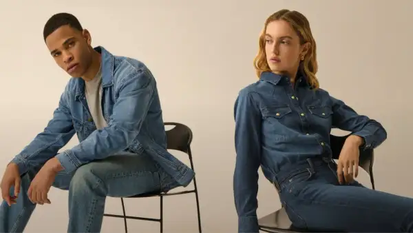 Coppia in total look denim. Lui con giacca e jeans, lei con camicia e jeans, entrambi con un fit che si stringe verso il basso, il tapered fit significato.