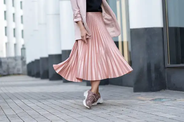 Gonna plissettata rosa cipria, un outfit inverno chic con blazer e sneakers.