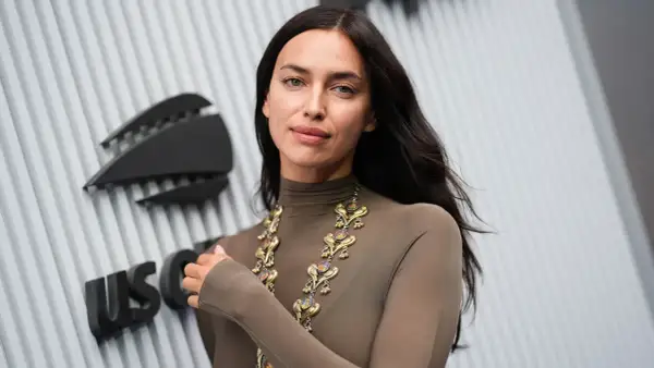 Irina Shayk, con un look audace e una collana d'oro, posa davanti a un logo.