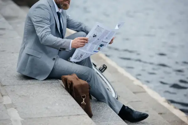 Uomo in vestito grigio legge il giornale, con scarpe nere eleganti. Un dilemma: vestito grigio che scarpe abbinare?