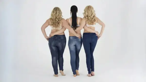 Tre donne in jeans e reggiseno, con le braccia incrociate sulla schiena. Un modo per far sembrare più alti.