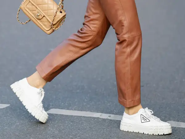 Un outfit chic con pantaloni in pelle marrone e sneakers bianche donna Prada. Una borsa Chanel completa il look.