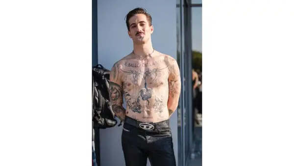 Damiano David, a torso covered in tattoos, poses confidently.