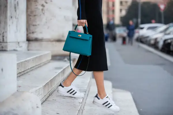 Scarpe da ginnastica bianche con strisce nere abbinate a un tubino nero e una borsa turchese.