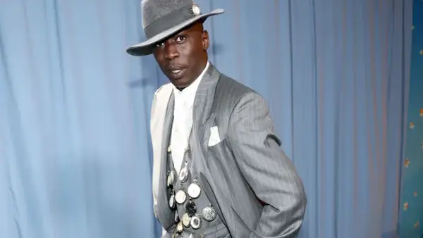 Un uomo con un cappello grigio e un completo gessato, ornato da numerosi orologi da taschino, incarna l'eleganza maschile.