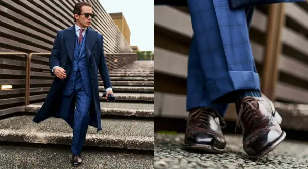 Uomo con outfit old money: completo blu a quadri, cappotto lungo, cravatta e scarpe stringate marroni.