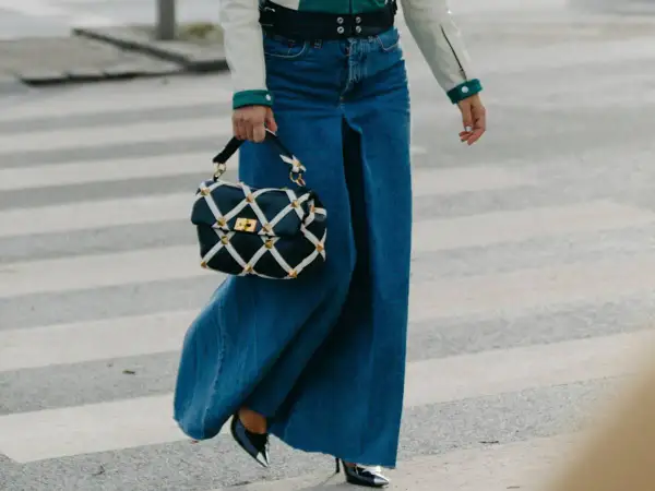 Un outfit gonna jeans lunga con borsa a tracolla trapuntata e tacchi lucidi, cammina su un attraversamento pedonale.