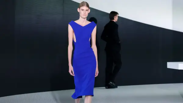 Modella con abito blu elettrico, un'opera di Simone Bellotti, sfila su una passerella minimalista.